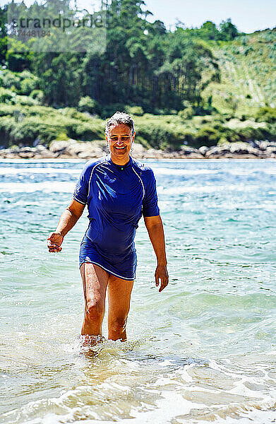 Frau mittleren Alters steigt am Strand aus dem Wasser