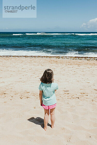 Junges Mädchen beobachtet Meereswellen von einem Strand in Oahu