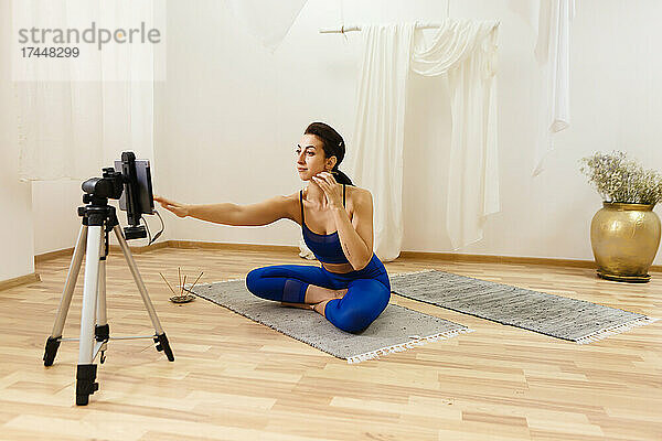 Yogatrainerin trainiert online per Smartphone auf einem Stativ