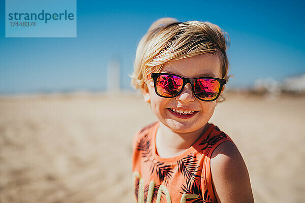 Glücklich lächelnder kleiner Junge mit Sonnenbrille am Strand