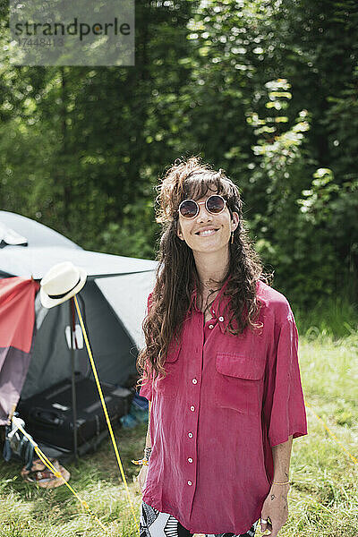 Lächelnde  glückliche  schöne Frau mit langen braunen Haaren und rosafarbenem Hemd beim Camping