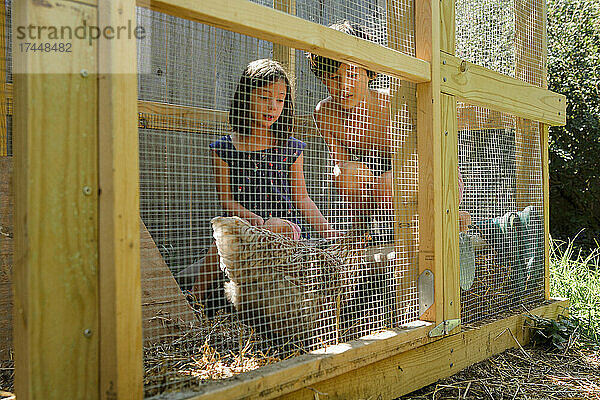 Zwei Kinder sitzen zusammen im Hühnerstall und spielen mit Hinterhofhühnern