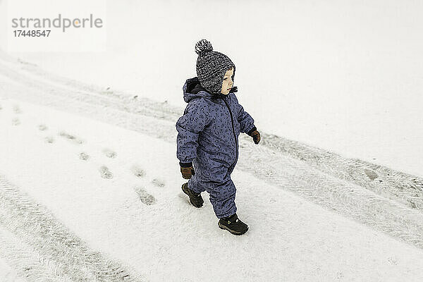 Kleiner Junge im blauen Strampler läuft selbstbewusst draußen im Schnee