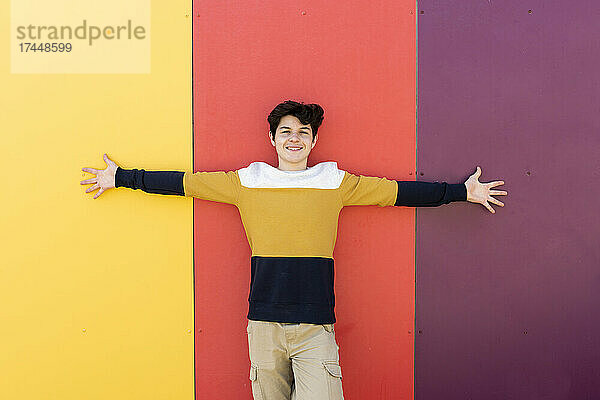 Glücklicher junger Mann mit ausgestreckten Armen gegen farbige Wand