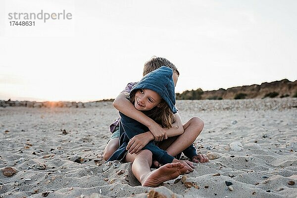 Bruder und Schwester umarmen sich am Strand bei Sonnenuntergang