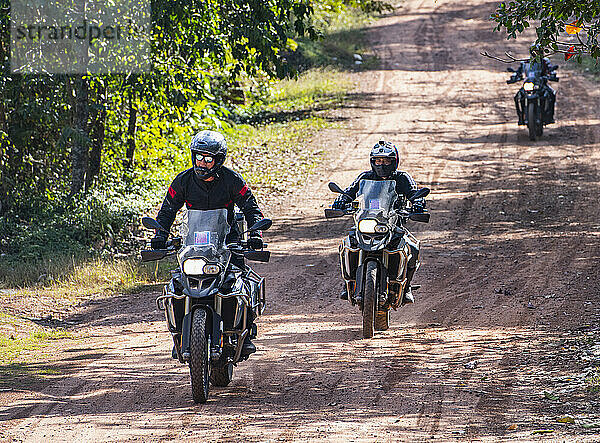 Männer fahren mit ihren Abenteuermotorrädern auf staubiger Straße in Kambodscha