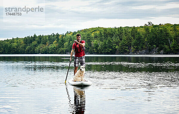 Mann paddelt mit seinem Hund auf einem See auf einem Stand-Up-Paddleboard-SUP.