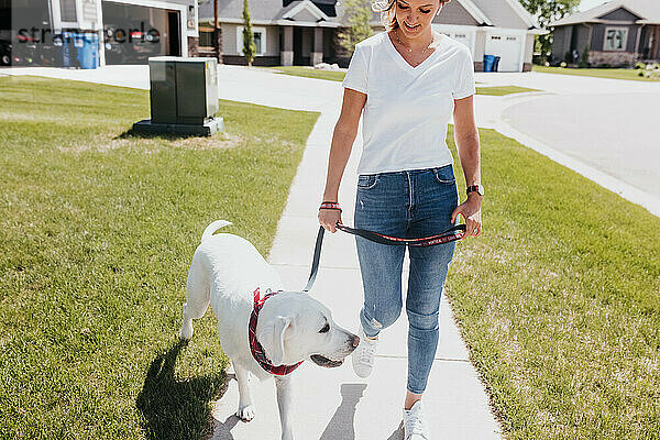 An einem sonnigen Tag geht eine Frau mit ihrem Hund durch die Nachbarschaft