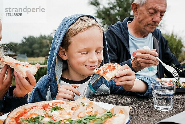 Junge isst glücklich Pizza mit seiner Familie draußen im Garten