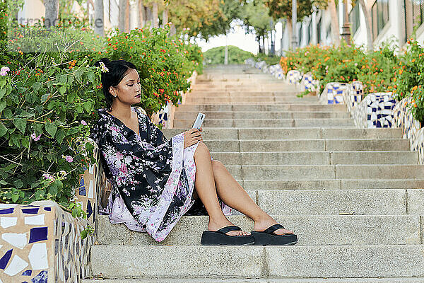 Eine junge asiatische Frau  die als Geisha verkleidet ist  schaut in einem Garten auf ihr Telefon