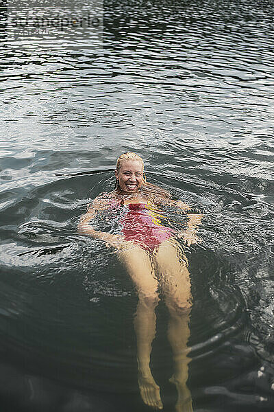 Lächelnde blonde Frau im bunten Badeanzug schwimmt im Sommer im See