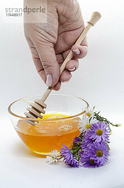 Die Hand einer Frau rührt den Honig mit einem Honiglöffel um