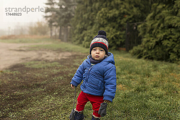 Kleiner Junge steht bei nebligem Wetter in Winterkleidung auf Gras