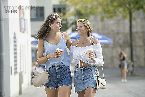 Zwei junge Frauen gehen mit Kaffeetassen durch die Münchner Innenstadt
