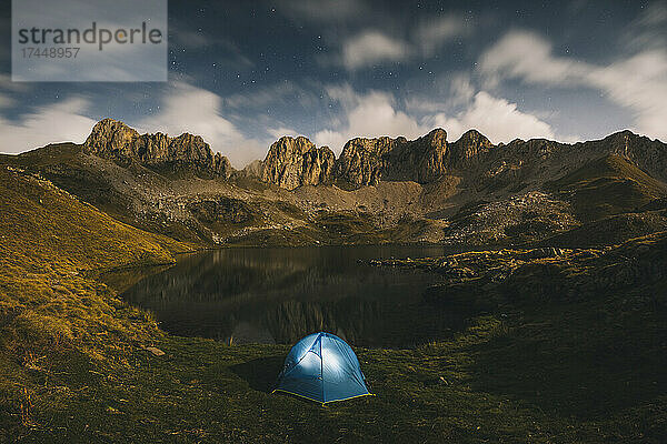 Beleuchtetes Zelt vor schroffen Bergen und See  Pyrenäen.