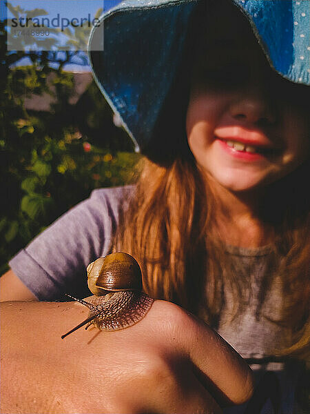 Junges lächelndes Mädchen mit einer Schnecke auf der Hand aus nächster Nähe