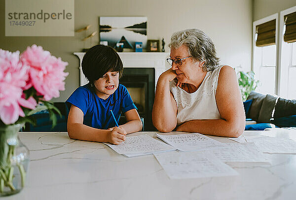 Großmutter hilft Enkel beim Hausaufgabenschreiben zu Hause.