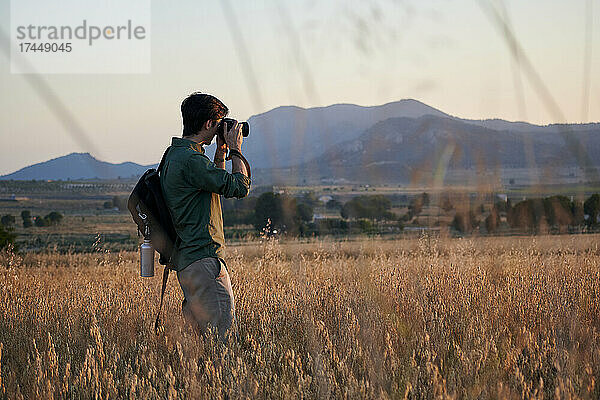 Ein Fotograf mit Rucksack macht bei Sonnenuntergang ein Foto auf einer Wiese