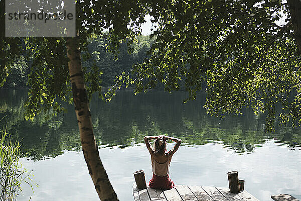 Junger Mensch entspannt sich im Sommer am Seeufer auf einem Holzsteg unter Bäumen