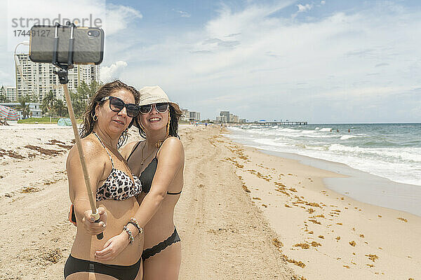Mutter und Tochter am Strand machen ein Foto mit ihrem Smartphone