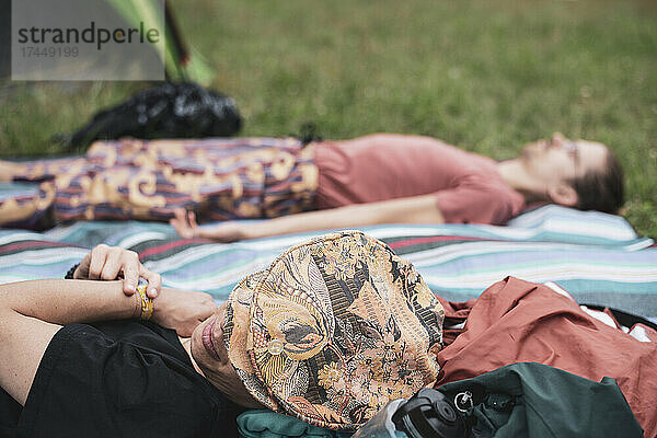 Zwei farbenfrohe queere Freunde entspannen sich auf einer Picknickmatte im Festivalcamp