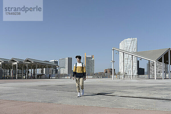 Vorderansicht eines jungen Mannes mit Rucksack  der an einem sonnigen Tag durch die Stadt spaziert
