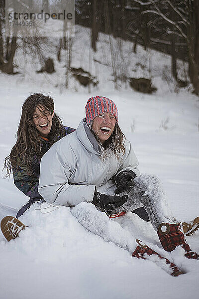 Freundinnen lachen  während sie auf der Rodelbahn mit Schnee bedeckt werden