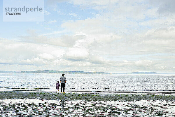 Weite Ansicht eines Vaters und einer Tochter  die zusammen am Strand stehen