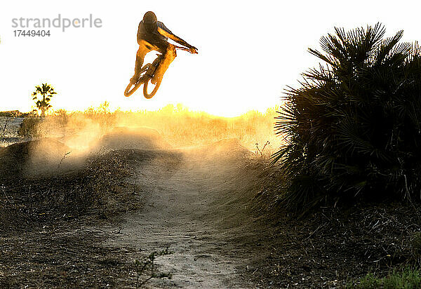 Junger Mountainbiker springt in einen windigen und staubigen Sonnenuntergang in Spanien