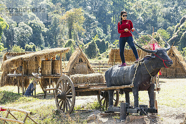 Frau posiert auf einer Stierskulptur im traditionellen Dorf in Thailand