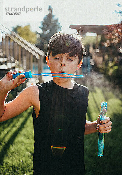 Kleiner Junge bläst an einem sonnigen Tag Seifenblasen in einem Hinterhof.