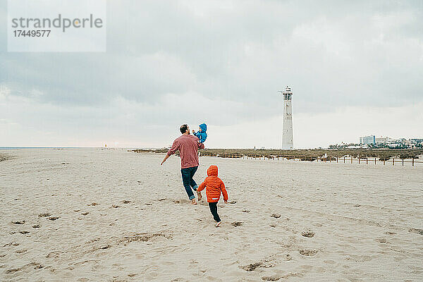 Vater und Kinder laufen an einem kalten  bewölkten Tag am Strand