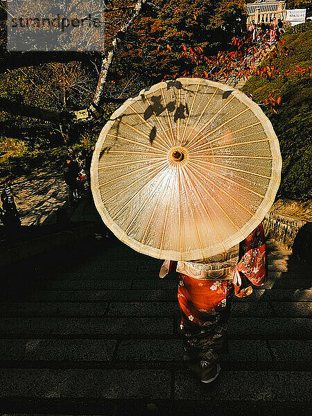 Frau trägt einen roten Kimono und hält einen traditionellen Regenschirm