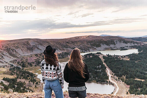 Rückansicht von zwei Frauen  die neben einem See mit Bergen stehen