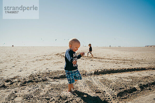 Kleiner Junge läuft glücklich am Kiterstrand auf Fuerteventura
