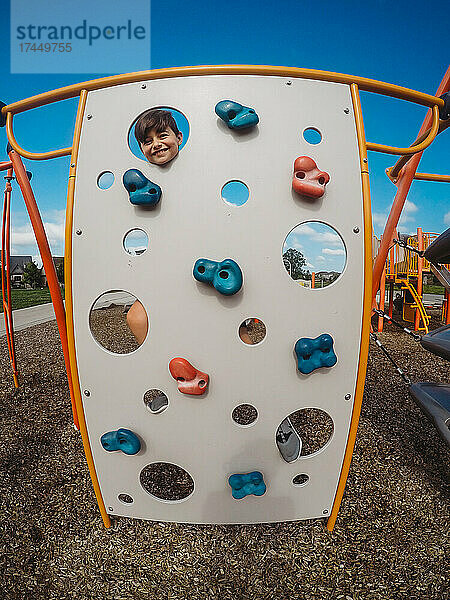 Fröhlicher Junge  der auf einem Spielplatz durch Löcher in einem Klettergerüst späht.