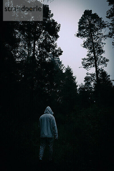 Ein Mann mit weißem Kapuzenpullover spaziert durch einen dunklen Wald
