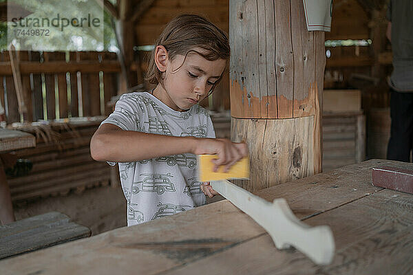 Ein konzentrierter Junge schleift das Holzschwert