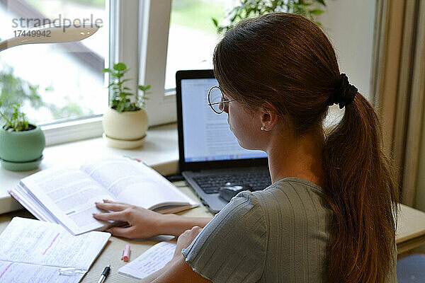 Studentin lernt zu Hause mit Büchern und Laptop