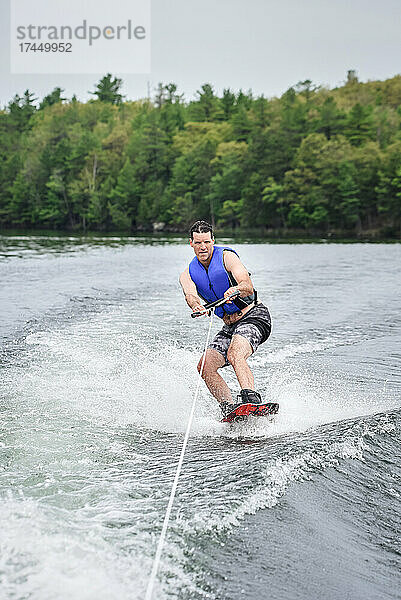 Mann beim Wakeboarden  während er von einem Boot auf einem See gezogen wird.