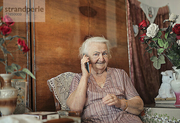 Porträt einer älteren Dame in ihrem Haus beim Telefonieren