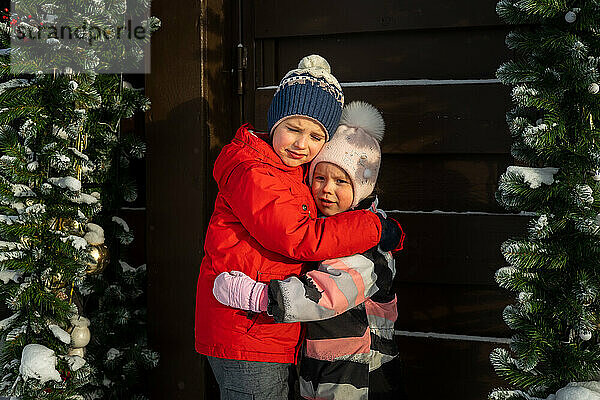 Zwei Kinder  Bruder und Schwester  umarmen sich im Winterdorf.