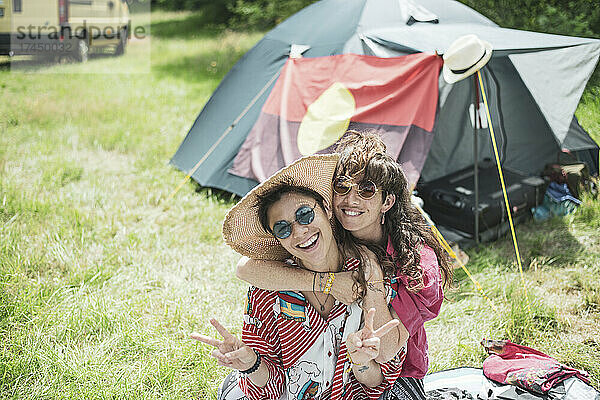 Lächelndes queeres Paar in bunten Kleidern beim Zelten auf dem Festival