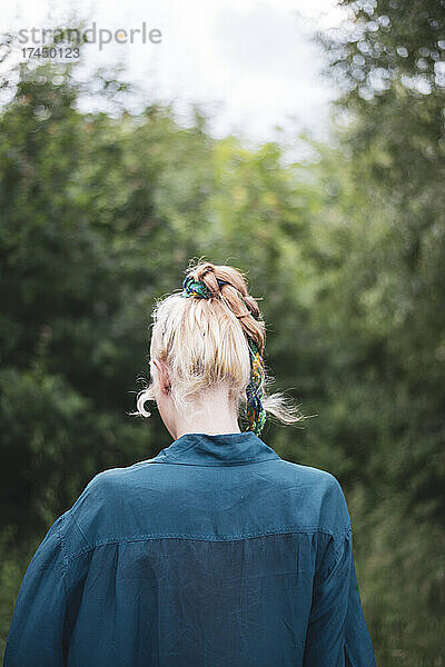 Blonde Frau mit böhmischer Frisur und blauem Hemd geht im Wald spazieren