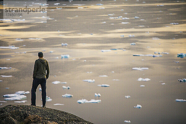 Rückansicht eines Mannes  der auf einer Klippe über dem Meer und Eisbergen steht.