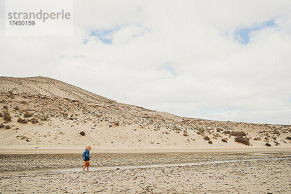 Kleines Kind läuft an einem kalten  bewölkten Tag zwischen Sanddünen am Strand
