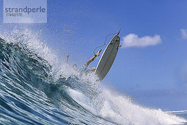 Mann mit Surfbrett surft auf Meereswelle vor klarem Himmel