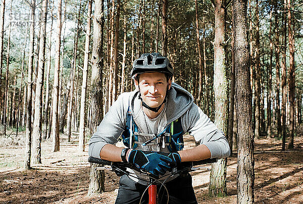 Porträt eines Mannes  der sich beim Radfahren im Wald auf sein Fahrrad stützt