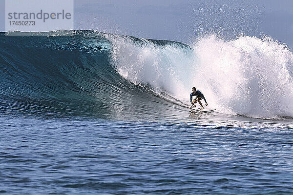 Mann mit Surfbrett surft auf Meereswelle vor klarem Himmel