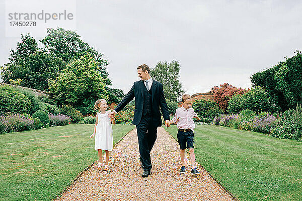 Vater und Kinder gehen bei einer Hochzeit durch ein Blumenfeld